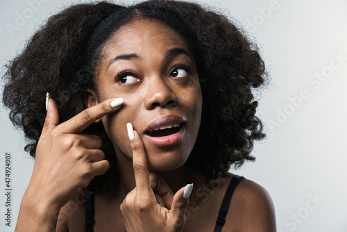 Young black woman in bra squeezing pimple on her face