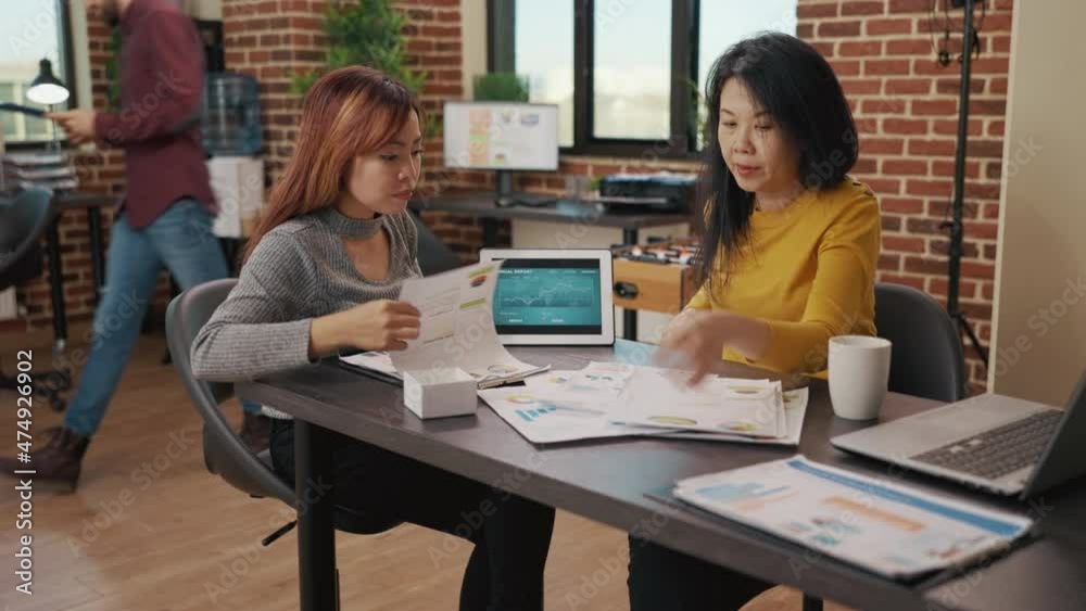Business women examining financial charts on digital tablet and papers to plan sales development in office. Company employees doing research with annual report and analysis for growth. Business women examining financial charts on digital tablet and papers to plan sales development in office. Company employees doing research with annual report and analysis for growth.