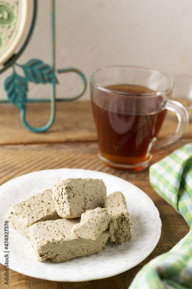 Several pieces of sunflower halva on a white saucer with a cup of tea on a wooden table in the kitchen. Rustic style. Traditional natural sweets. Vetikal orientation. Several pieces of sunflower halva on a white saucer with a cup of tea on a wooden table in the kitchen. Rustic style. Traditional natural sweets. Vetikal orientation.