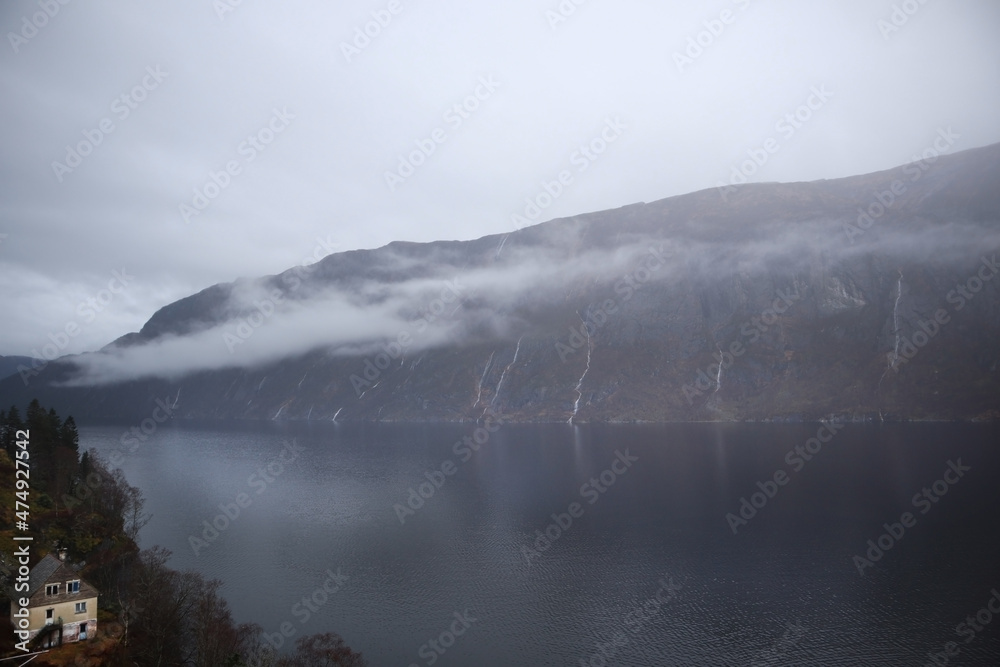 View of the Norwegian lake river in cloudy rainy weather through the trees. Resting place near the river lake. Mountain view in Norway.
