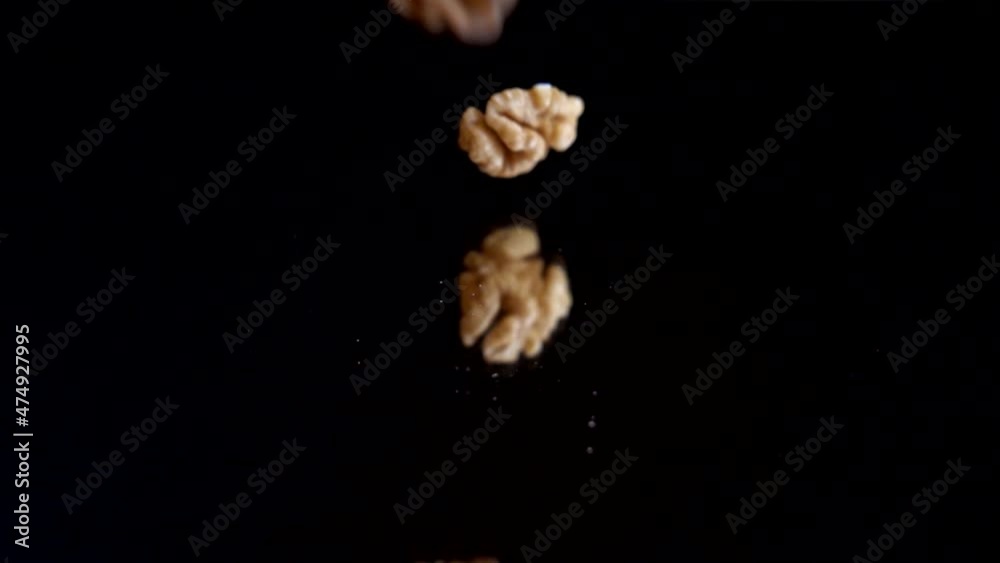 Walnut kernels fall on a black mirror surface. Slow motion. Juglans regia. Walnut kernels fall on a black mirror surface. Slow motion. Juglans regia.