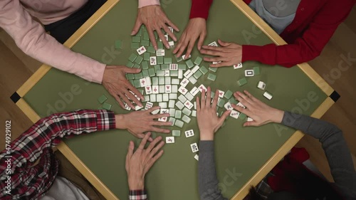 top angle shot with cropped view of family's hands mixing the face-down mahjong pieces on green table while playing tile game on chinese lunar new year's eve at home
