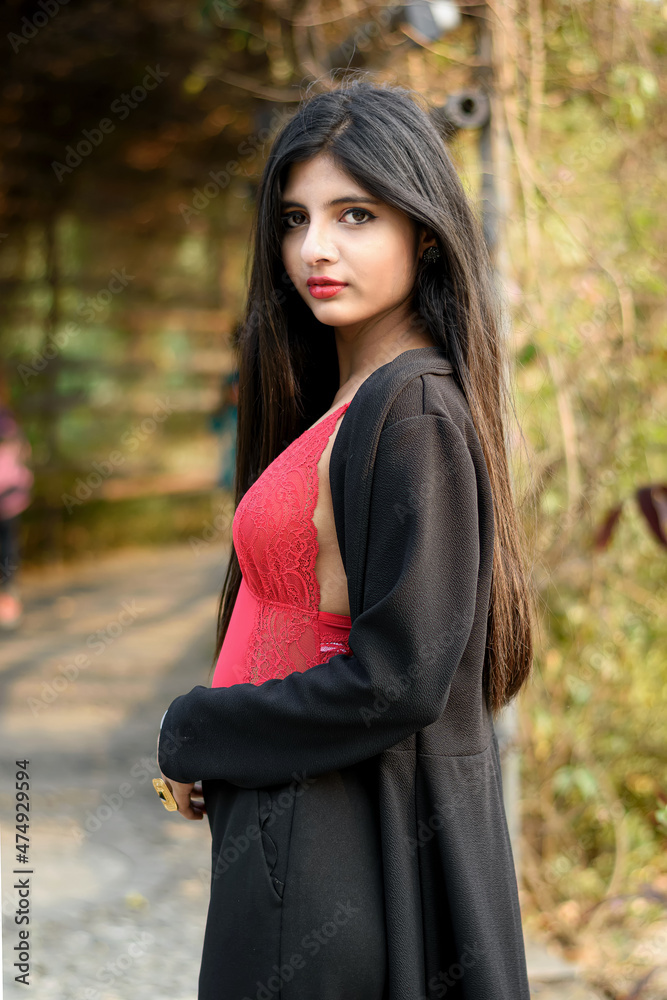 Portrait of very beautiful attractive Indian woman wearing red outfit with black jacket posing in front of tropical green leaves on a sunny day in a blurred green background. Lifestyle and Fashion. Portrait of very beautiful attractive Indian woman wearing red outfit with black jacket posing in front of tropical green leaves on a sunny day in a blurred green background. Lifestyle and Fashion.