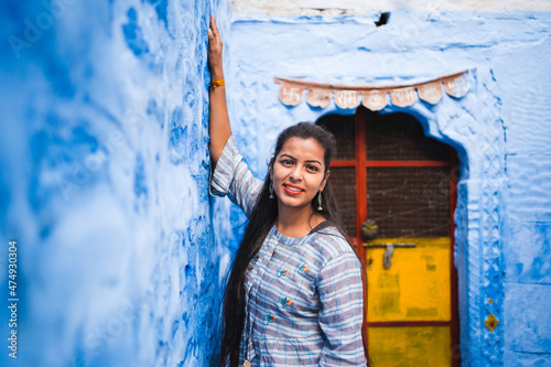 Beautiful Indian female model at blue district Chandpole of the old city in Jodhpur, Rajasthan, India. Attractive girl with long hair in modern clothes, blue jeans and blue background.  © Irina