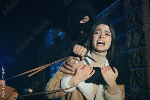 Criminals threatening young woman with knife outdoors at night. Self defense concept