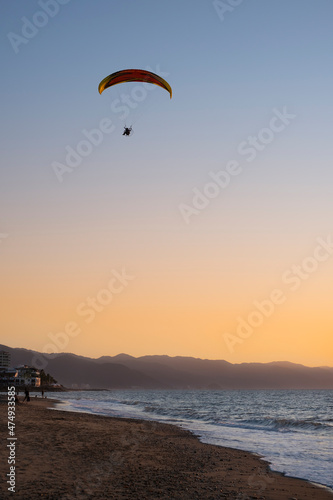 Motor hang glider flying high in the air over the beach and ocean at sunset hour. Sport and recreation concept.