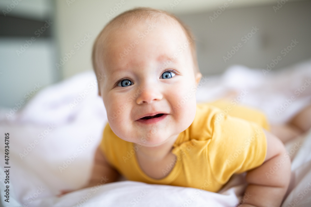 Caucasian blonde baby seven months old lying on bed at home. Kid wearing cute clothing trendy colors: illuminating yellow. Infant playing with toys Caucasian blonde baby seven months old lying on bed at home. Kid wearing cute clothing trendy colors: illuminating yellow. Infant playing with toys