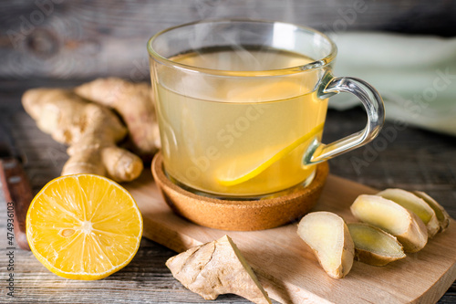 Glass cup of hot ginger tea with lemon slice on a wooden cutting board. Natural organic antiflu ingredients, alternative medicine, immune support. Energy and vitality tonic drink.
