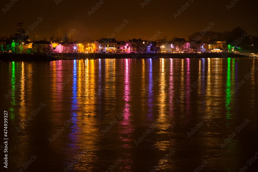 Quai devant un fleuve, la Loire, éclairé par les lumières colorées de Noël se reflétant dans l'eau. Trentemoult à Rezé, France. Photo en pose longue