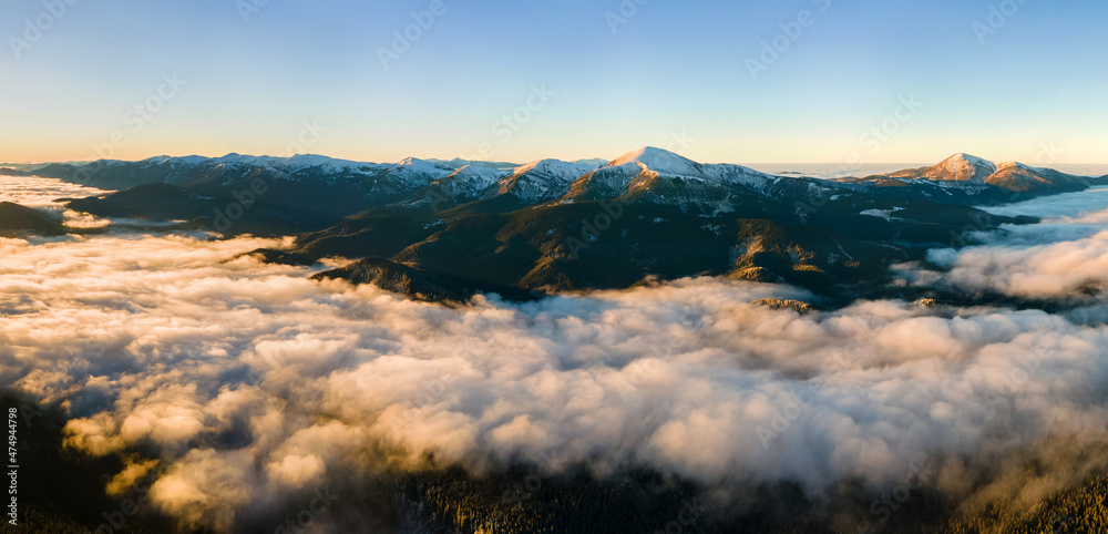 Aerial view of vibrant sunrise over white dense fog with distant dark Carpathian mountains on horizon