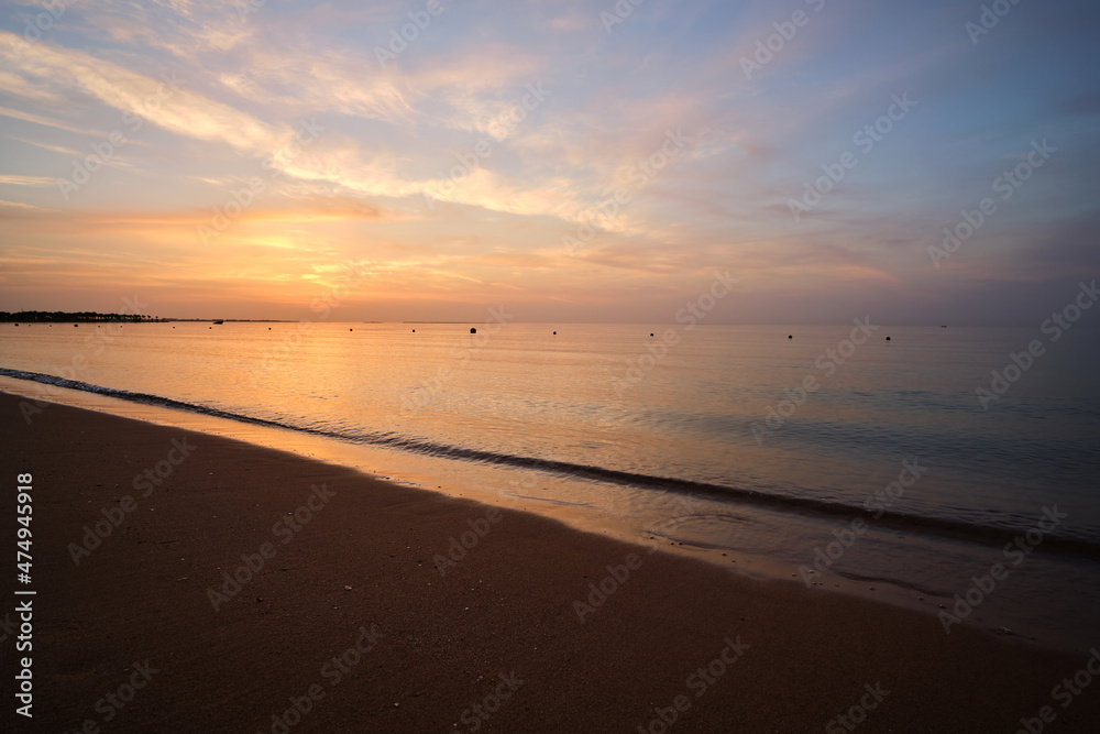 Calm sea shore with crushing waves on sandy beach at sunrise