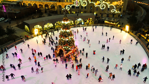 Top view of people skate on ice rink around christmas tree in park on winter holidays. Active healthy lifestyle entertainment for family and kids outdoor. Ice Skating. Soft focus