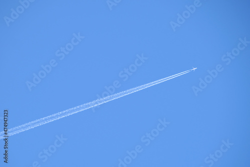 Distant passenger jet plane flying on high altitude on clear blue sky leaving white smoke trace of contrail behind. Air transportation concept © bilanol