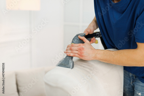 Worker from cleaning company vacuuming a white armchair