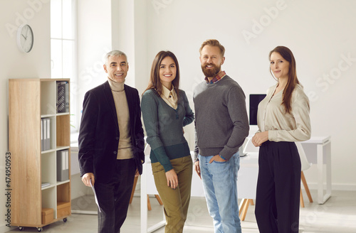 Small startup business team photo. Group portrait of successful and creative business team smiling confidently looking at camera. Women and men of different ages stand together in row in office.