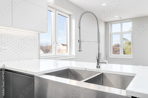 A stainless steel apron sink with a marble counter top  chrome faucet  and a view towards an empty living room.