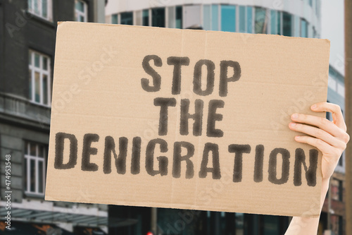 The phrase " Stop the denigration " on a banner in men's hand with blurred background. Harassment. Cruelty. Distrust. Cyberbulling. Victim. Separation. Suffer. Suffering. Trauma © AndriiKoval