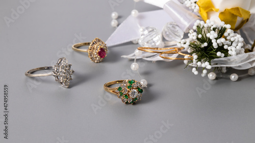 Beautiful gold rings with sparkling diamonds, ruby and emeralds on a gray background. Isolated jewelry. 