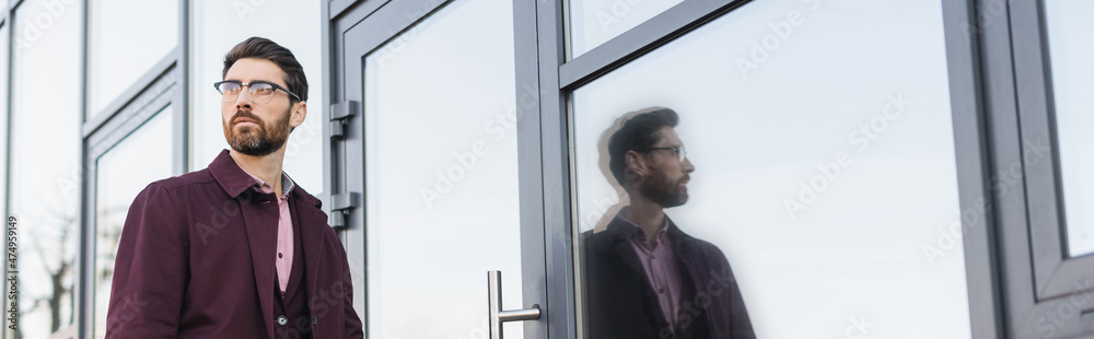 Fototapeta premium Businessman in trench coat walking near building on urban street, banner.