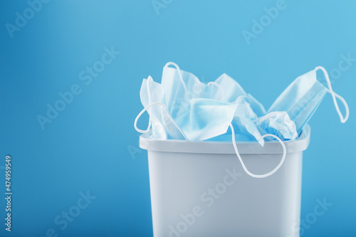 Waste bin full of used protective masks on a light blue background with free space.