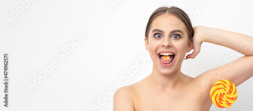 Happy expression young nude woman with candy in mouth holds lollipop near armpit on white background, epilation, depilation, hair removal concept