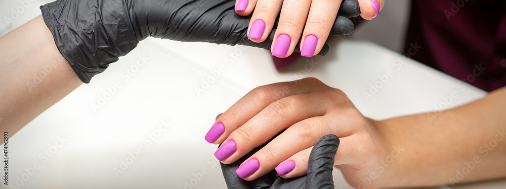 Examination of manicured fingernails. Hands of manicure master in black gloves examining female pink nails in manicure salon