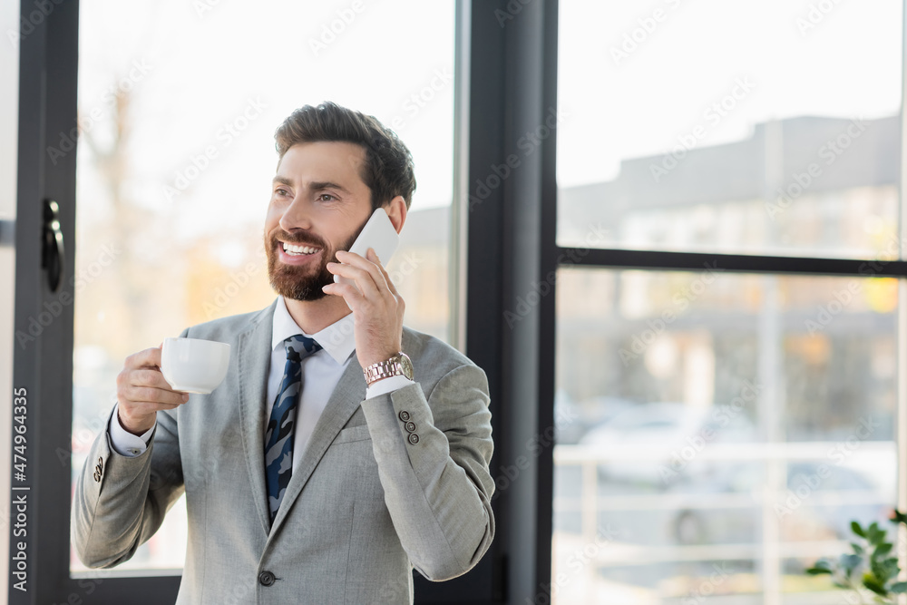 Smiling businessman talking on mobile phone and holding cup in office. Smiling businessman talking on mobile phone and holding cup in office.