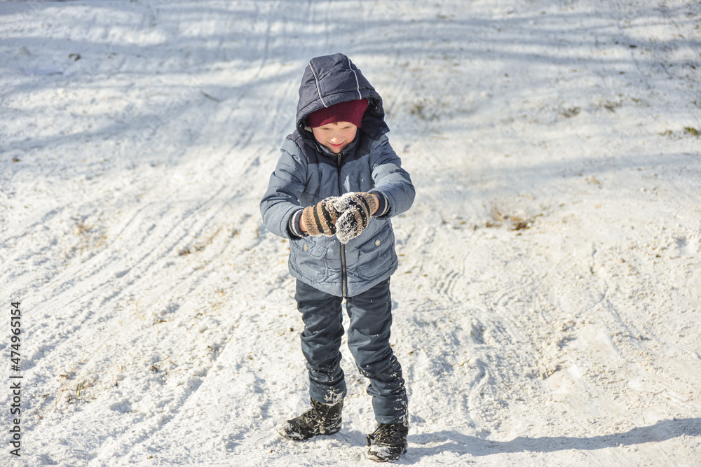 The boy straightens his mittens in the snow after playing snowballs.