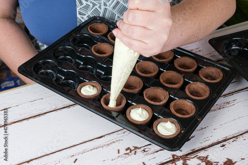 Selective focus. Confectioner filling with white chocolate ganache mini chocolate tarts. photo