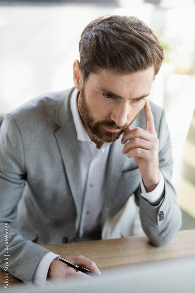 Businessman in formal wear holding pen near blurred computer in office. Businessman in formal wear holding pen near blurred computer in office.