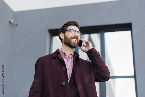 Businessman in trench coat talking on mobile phone on urban street.