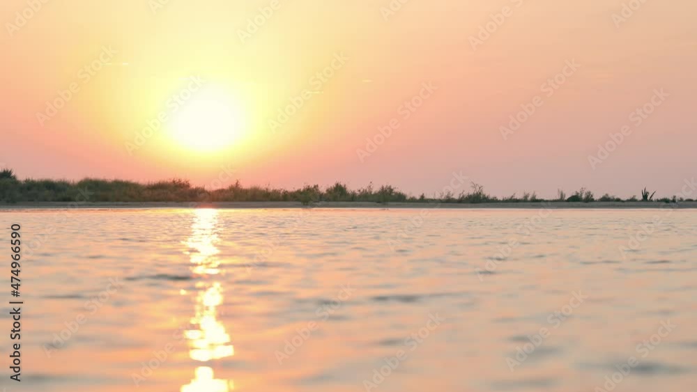 Beautiful sunrise over the river flowing into the sea. Sunbeams of yellow and orange colors reflected in the water. Scenic landscape of sunrise over the water. Beautiful sunrise over the river flowing into the sea. Sunbeams of yellow and orange colors reflected in the water. Scenic landscape of sunrise over the water.