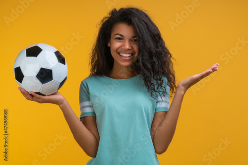 Attactive smiling girl soccer player or supporter is posing with a ball in hands isolated over bright colored yellow background © wpadington