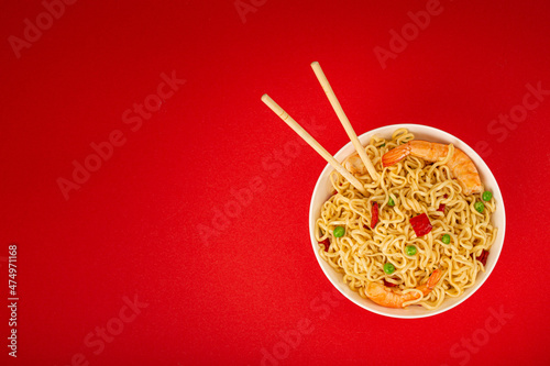 Asian Chinese noodles top view flat lay with shrimps and vegetables in white bowl with wooden sticks on red minimal paper background, minimal foodphoto concept, space for text photo