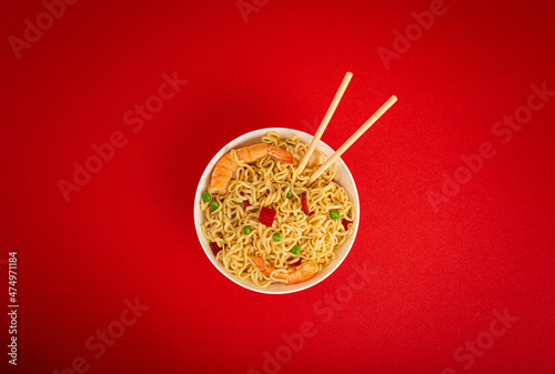 Asian Chinese noodles top view flat lay with shrimps and vegetables in white bowl with wooden sticks on red minimal paper background, minimal foodphoto concept  photo