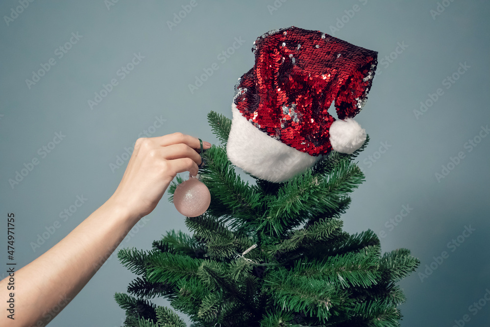 Women's hands decorate the Christmas tree with balls and toys. Red Santa Claus Hat on Christmas tree