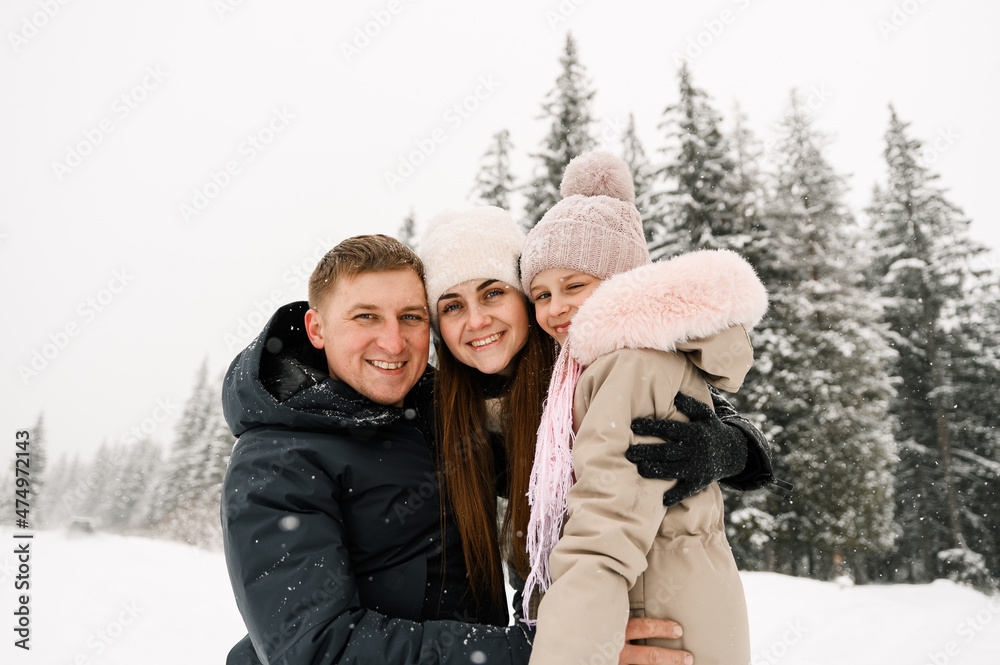 Obraz premium Portrait of playful happy family in winter forest. Mother, father and dauther playing with snow. Enjoying spending time together. Family concept