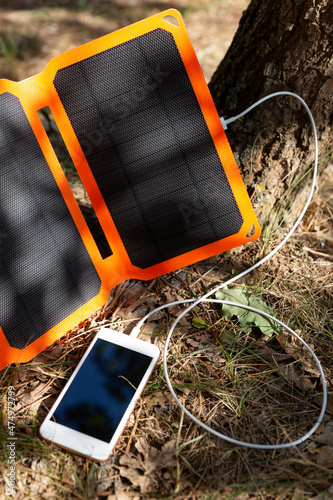 Smartphone is charging from solar battery in summer camp. Clean energy for using in hiking.
