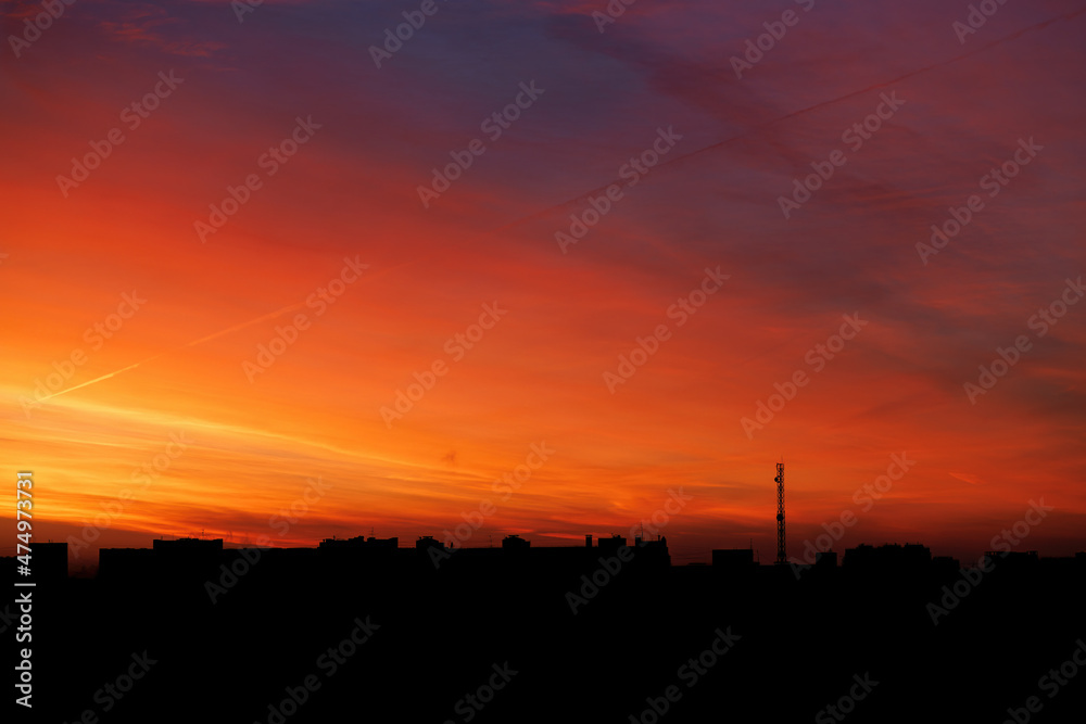 The sunrise is fiery red-orange over the silhouette of the city.