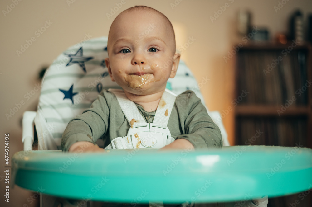 Baby eating with a face stained in food while in a child's dining chair Baby eating with a face stained in food while in a child's dining chair
