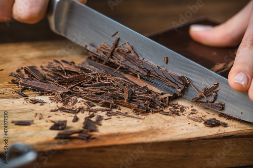 Cook cuts chocolate with a knife on a wooden table.