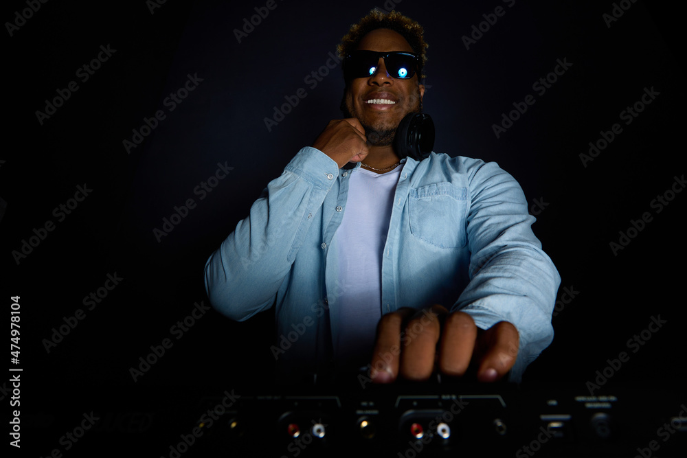 Happy African-American DJ with an Afro hairstyle plays music with  sunglasses. Black man DJ holds a party with headphones and a mixer. Hands  tuning musical equipment. Stock Photo | Adobe Stock