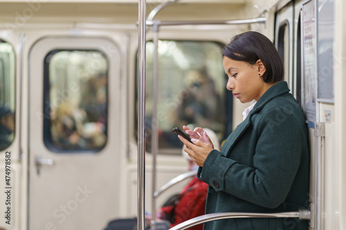 Young african girl addicted from social media scrolling mobile app while riding in subway to work or home. Black female in underground carriage holding smartphone and browse web, read email or texting