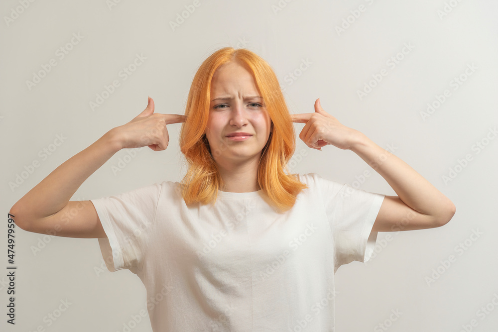 teen girl with red hair in a white t-shirt on a light background cover her ears with her hands teen girl with red hair in a white t-shirt on a light background cover her ears with her hands