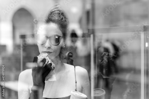 portrait of a cheerful young elegant caucasian woman wearing a tube black dress , having a croissant and a coffee for breakfast in a violin shop photo