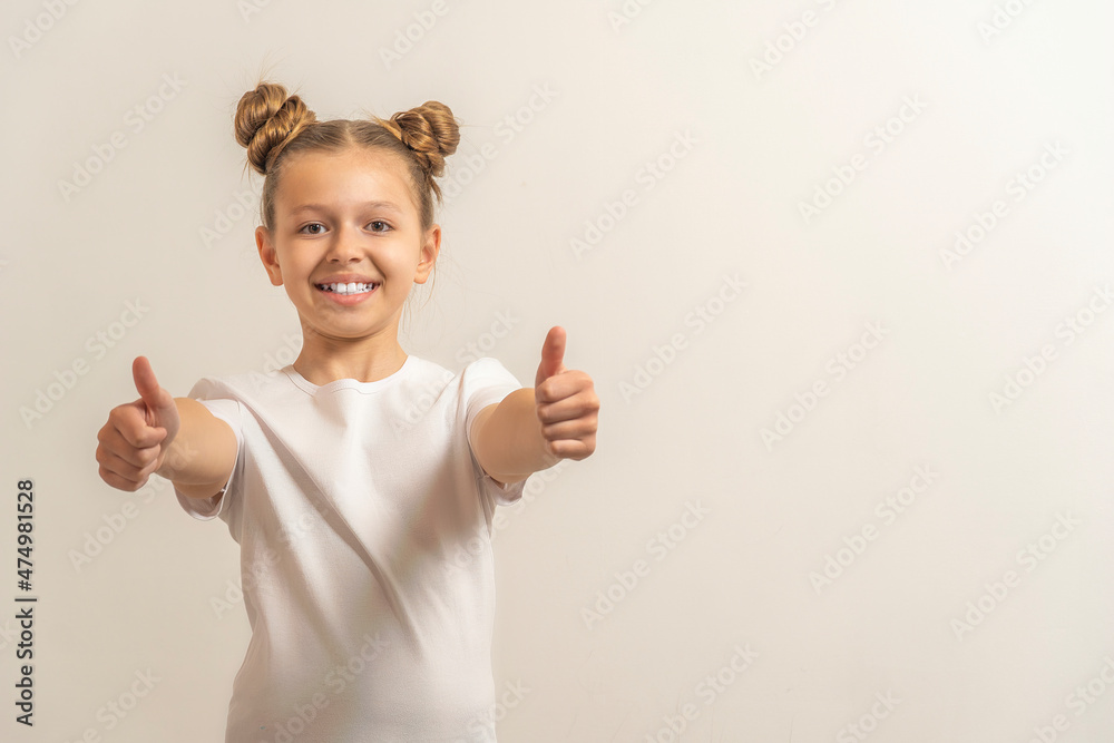 teenage girl with dark hair hair in a white t-shirt on a light background keep thumbs up gesture