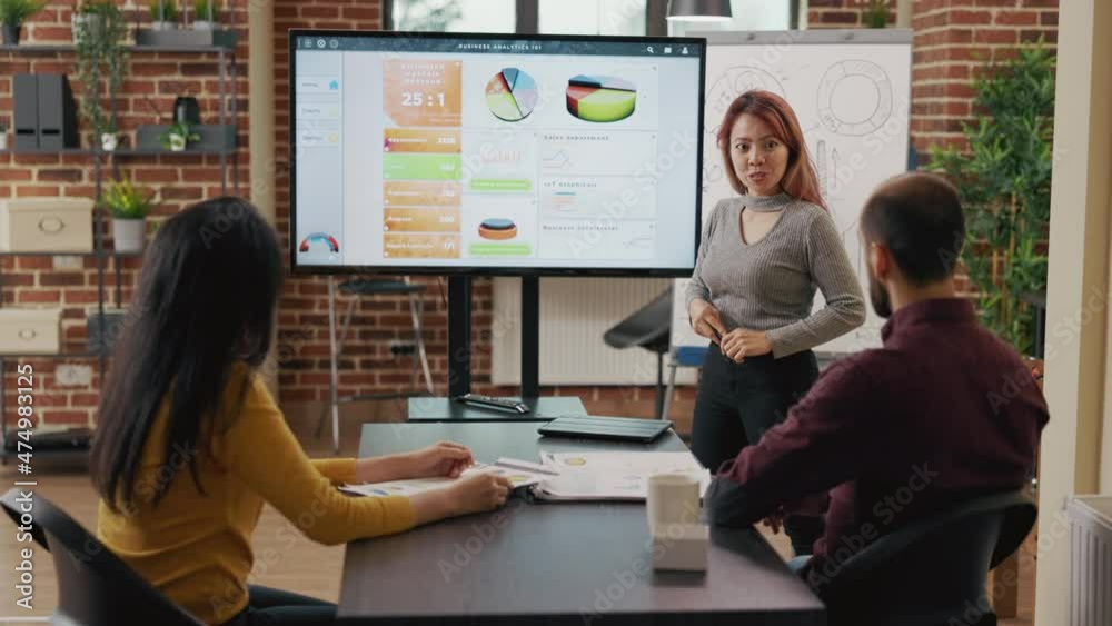 Asian woman explaining creative ideas to business people, meeting to work on presentation development. Colleagues discussing company growth with data graphics on monitor. Partnership Asian woman explaining creative ideas to business people, meeting to work on presentation development. Colleagues discussing company growth with data graphics on monitor. Partnership