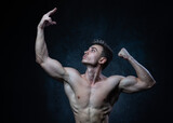 Young male athlete bodybuilder aestheticist posing against a dark background. Healthy lifestyle and sports concept.