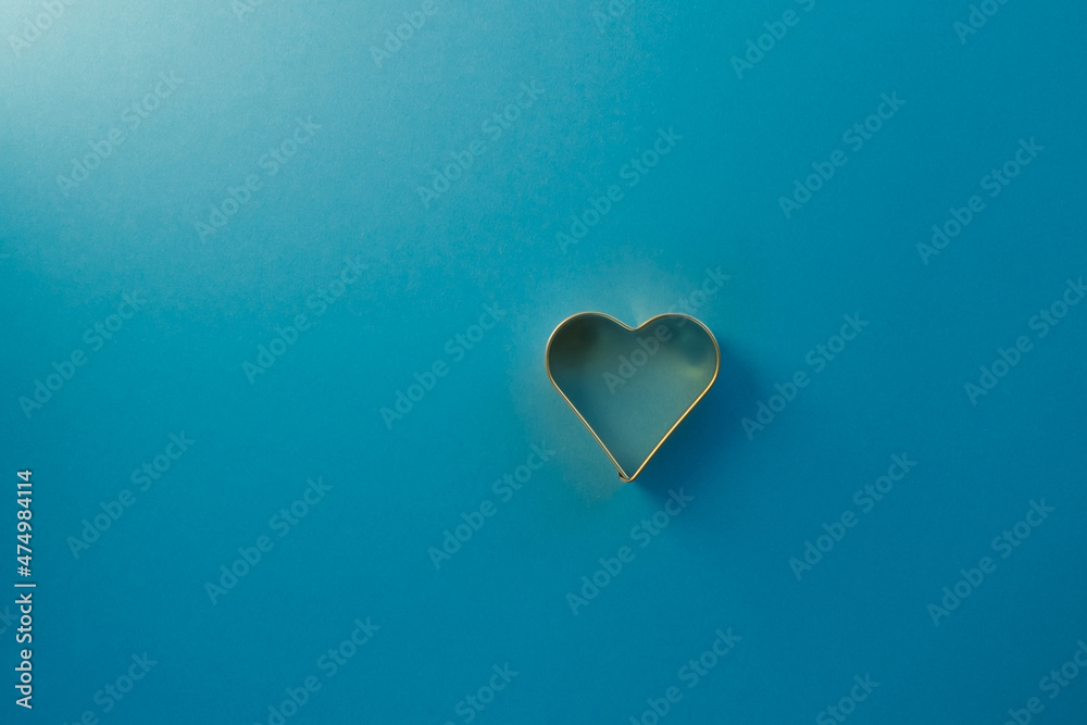 Golden heart-shaped mold on a harmonious azure background. Valentine's day concept, enamored hearts. Copy space view Golden heart-shaped mold on a harmonious azure background. Valentine's day concept, enamored hearts. Copy space view