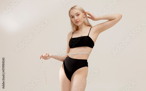 a slender girl in a swimsuit measures her waist with a centimeter